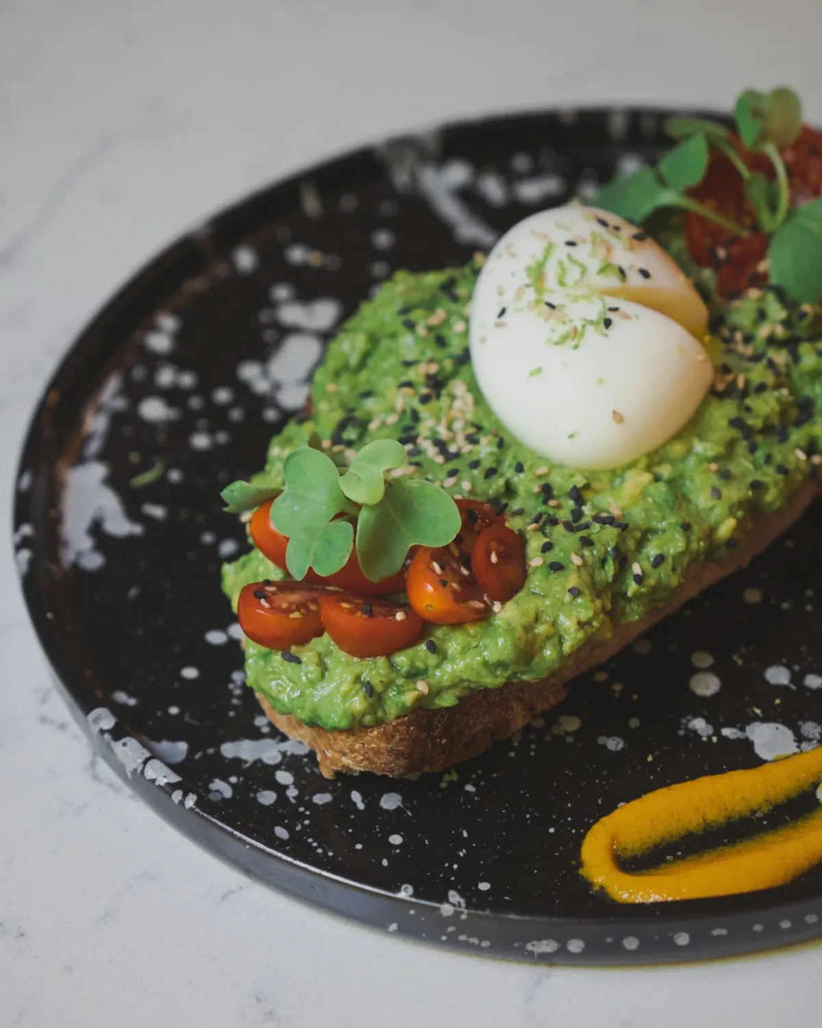 Avocado toast with egg, cherry tomatoes and sprouts, on a black plate