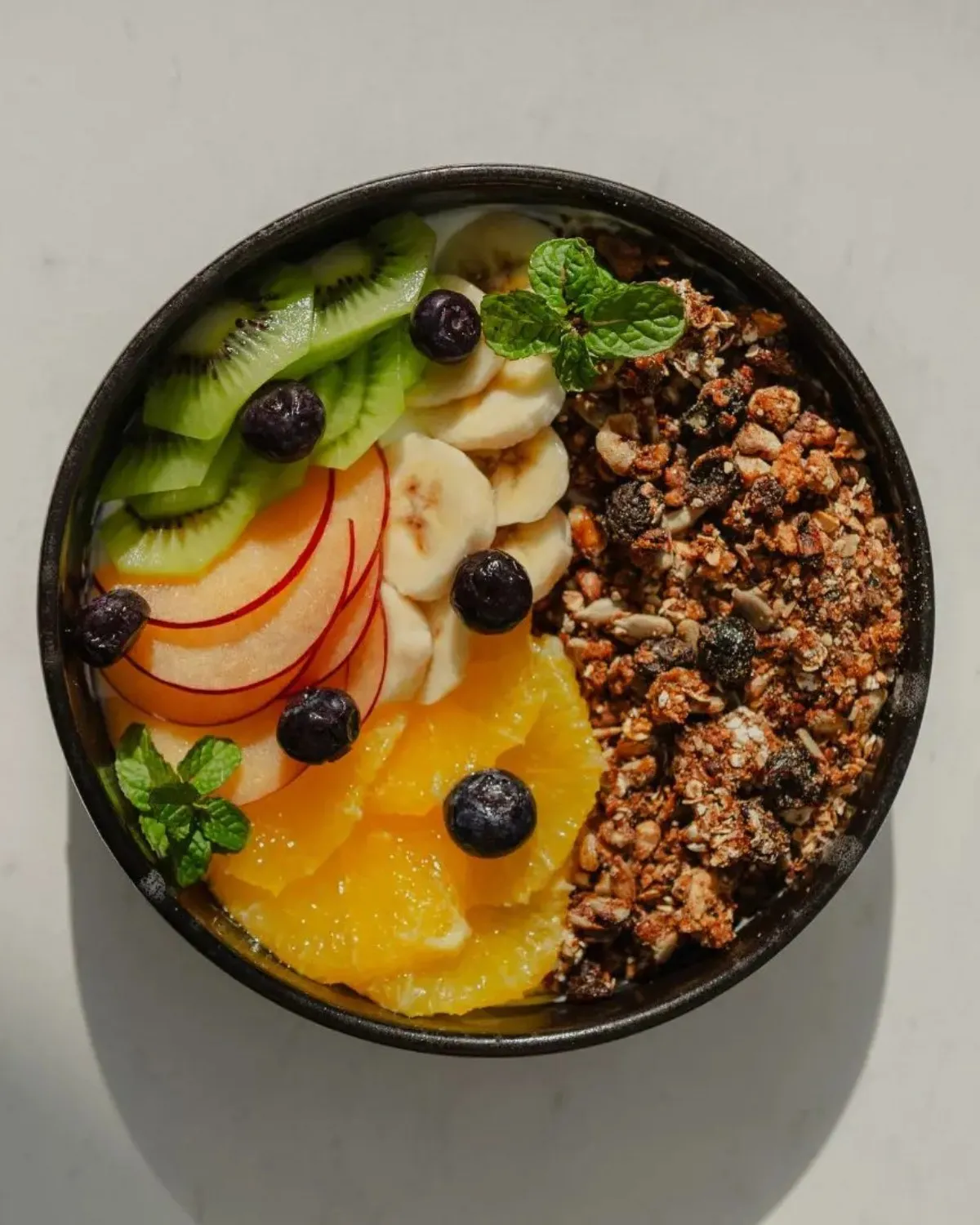 Seasonal fruit bowl with granola, blueberries and mint, seen from above